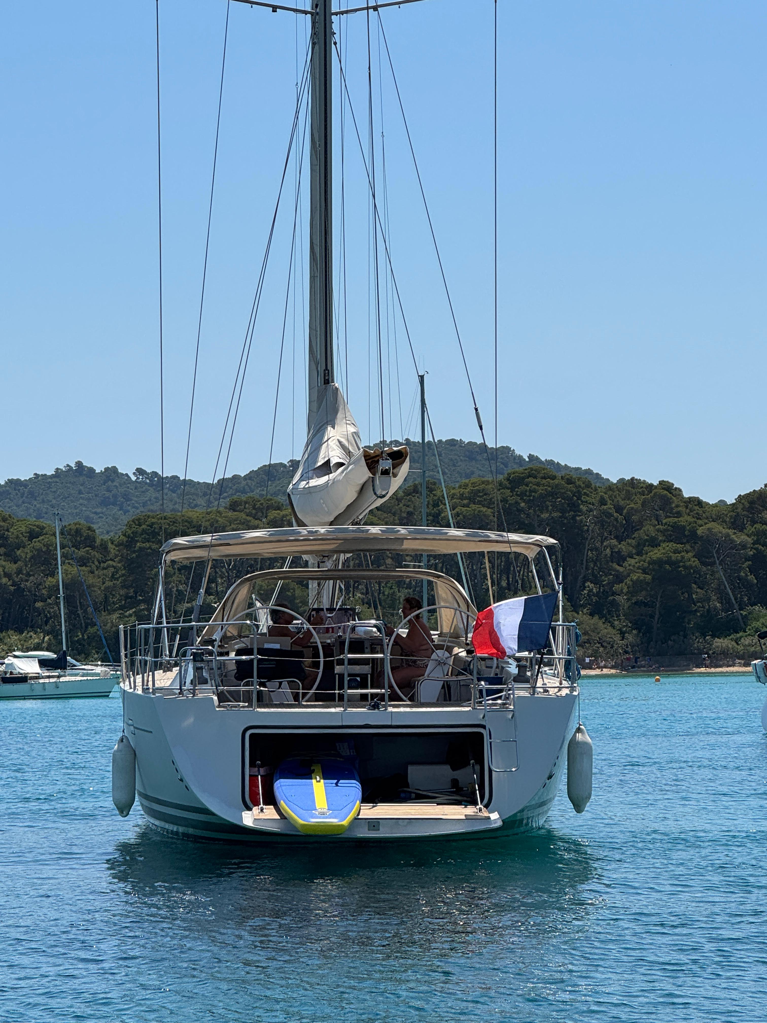 Voilier ancré dans une crique turquoise de Porquerolles, drapeau français